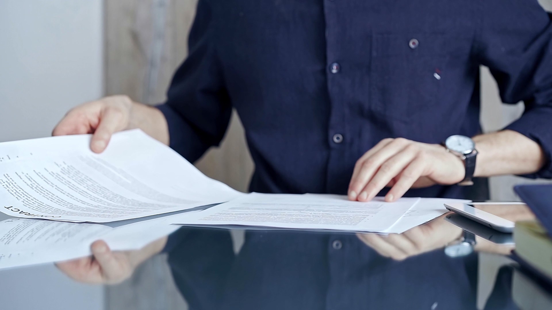 Businessman in dark blue t-shirt analyzing document at desk. Close-up of a professional auditor or lawyer reviewing a lengthy paper report in office setting. Business people concept